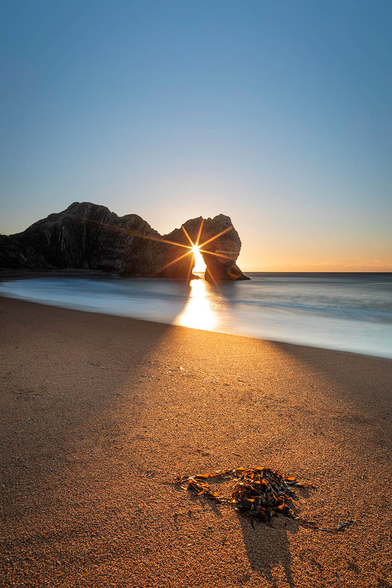 Sunburst through Durdle Door arch at sunrise, Dorset, Jurassic coast, England.
